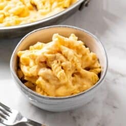 A bowl of cottage cheese mac and cheese on the table with a skillet of more in the background.