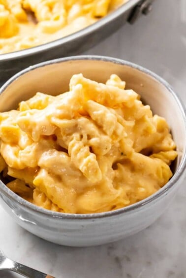 A bowl of cottage cheese mac and cheese on the table with a skillet of more in the background.