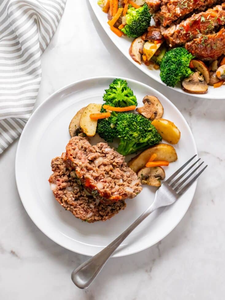 Slices of healthy meatloaf served up on a plate with vegetables and potatoes on the side.