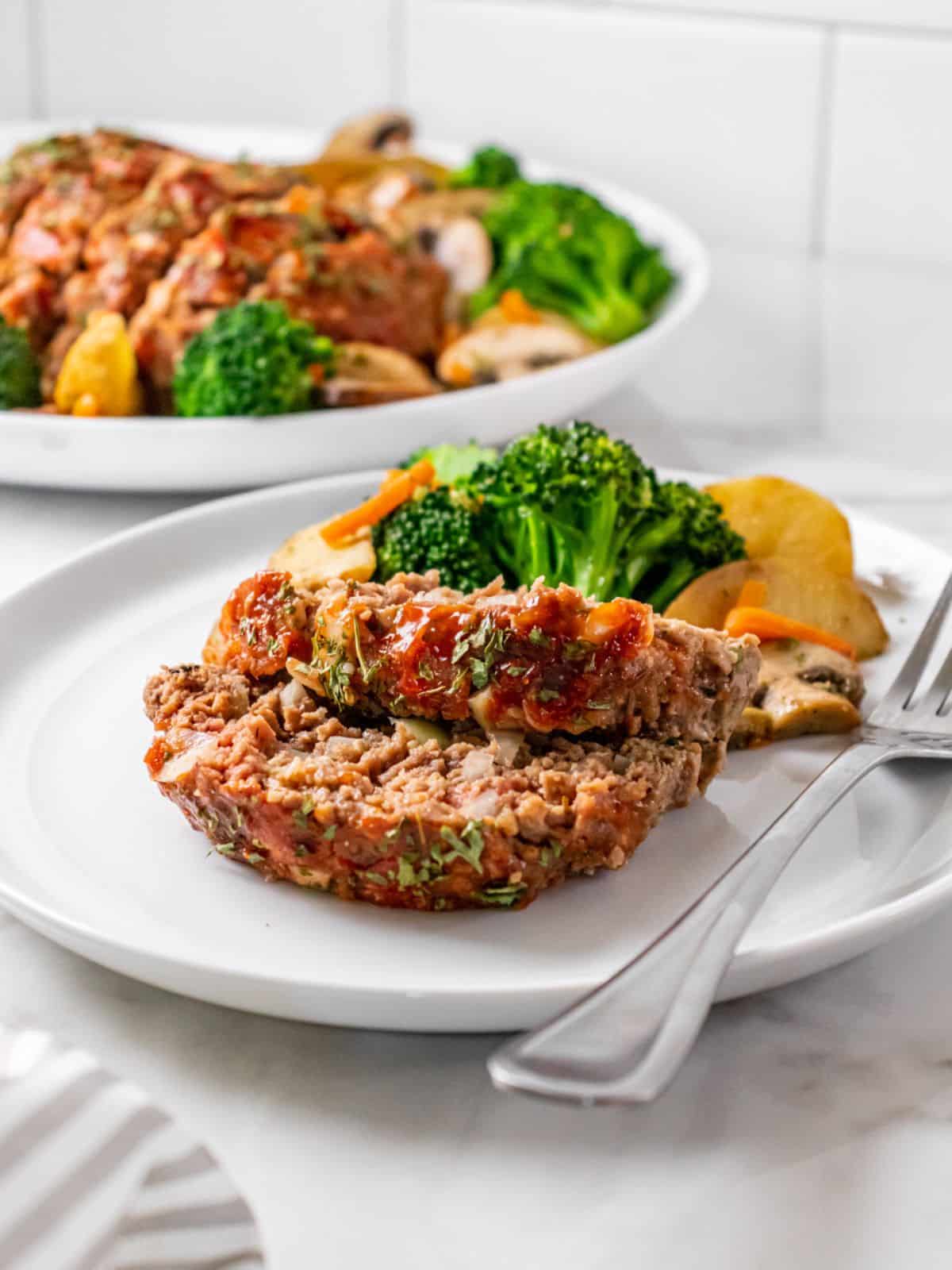 Two slices of beef meatloaf on the table with the platter of meatloaf in the background.