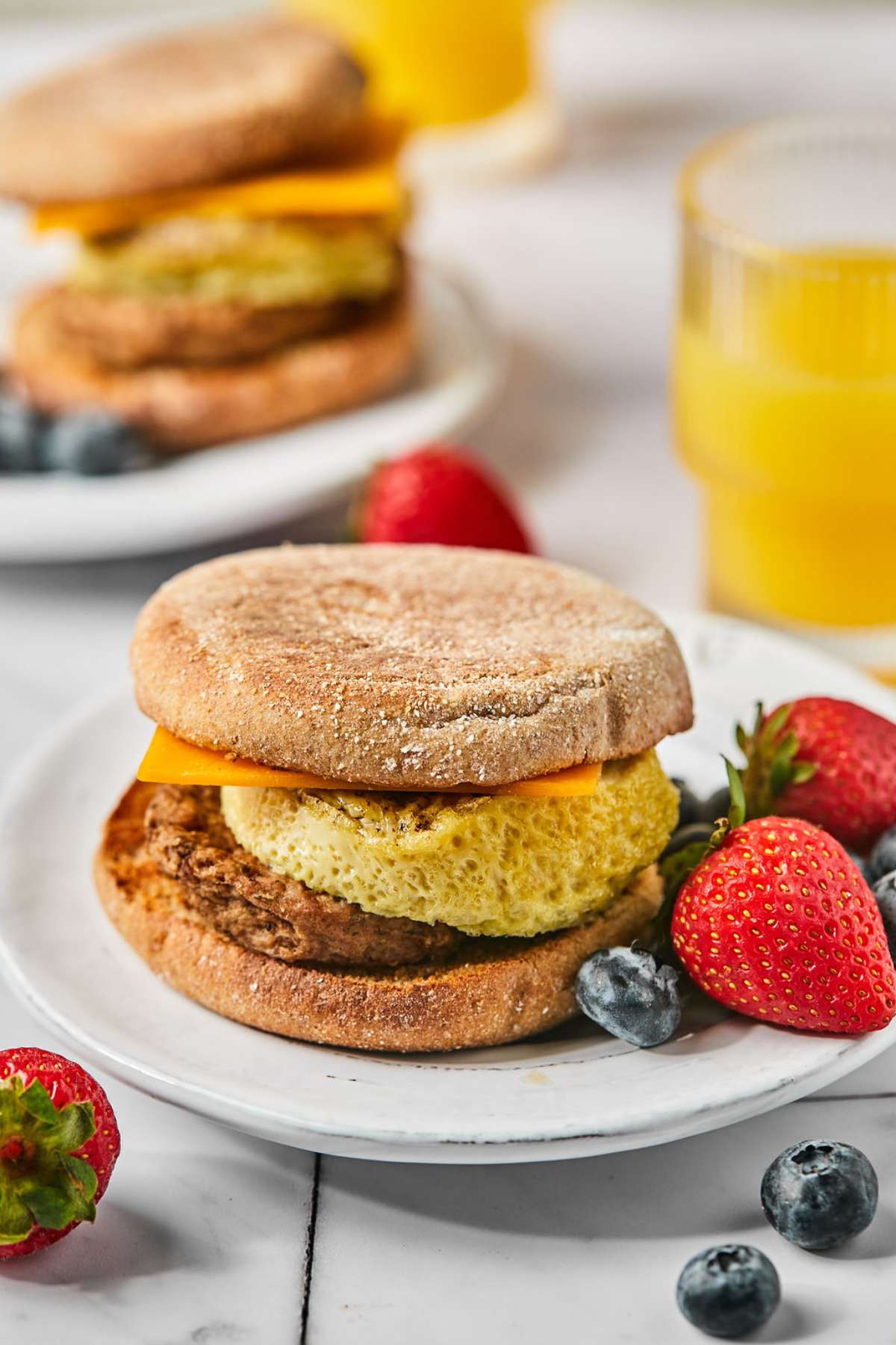 High protein breakfast sandwich on a plate with fruit and a glass of orange juice.