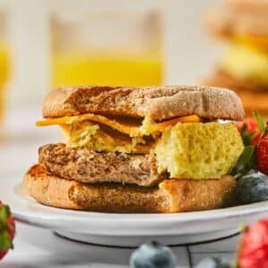 High protein breakfast sandwich on a plate with a bite missing and some fresh fruit on the side.