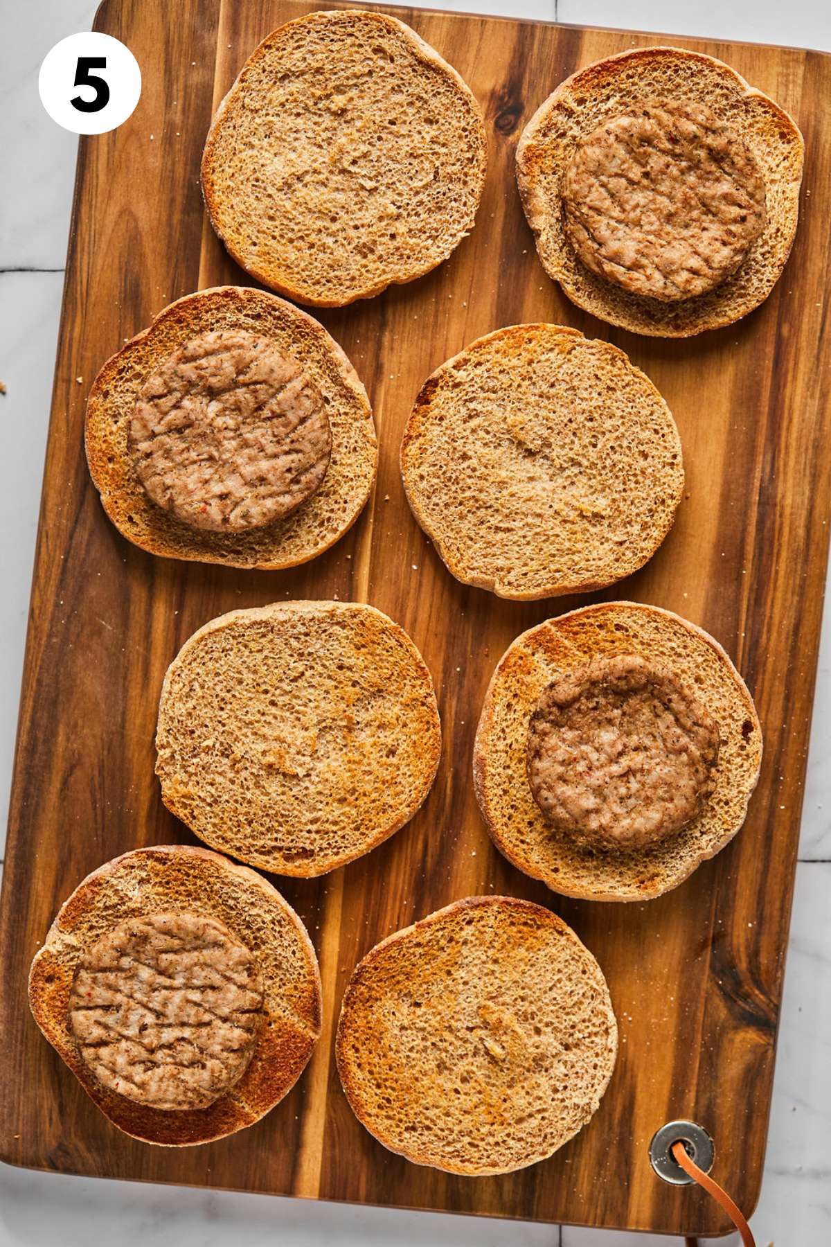 Muffins opened on a cutting board and half topped with sausages.