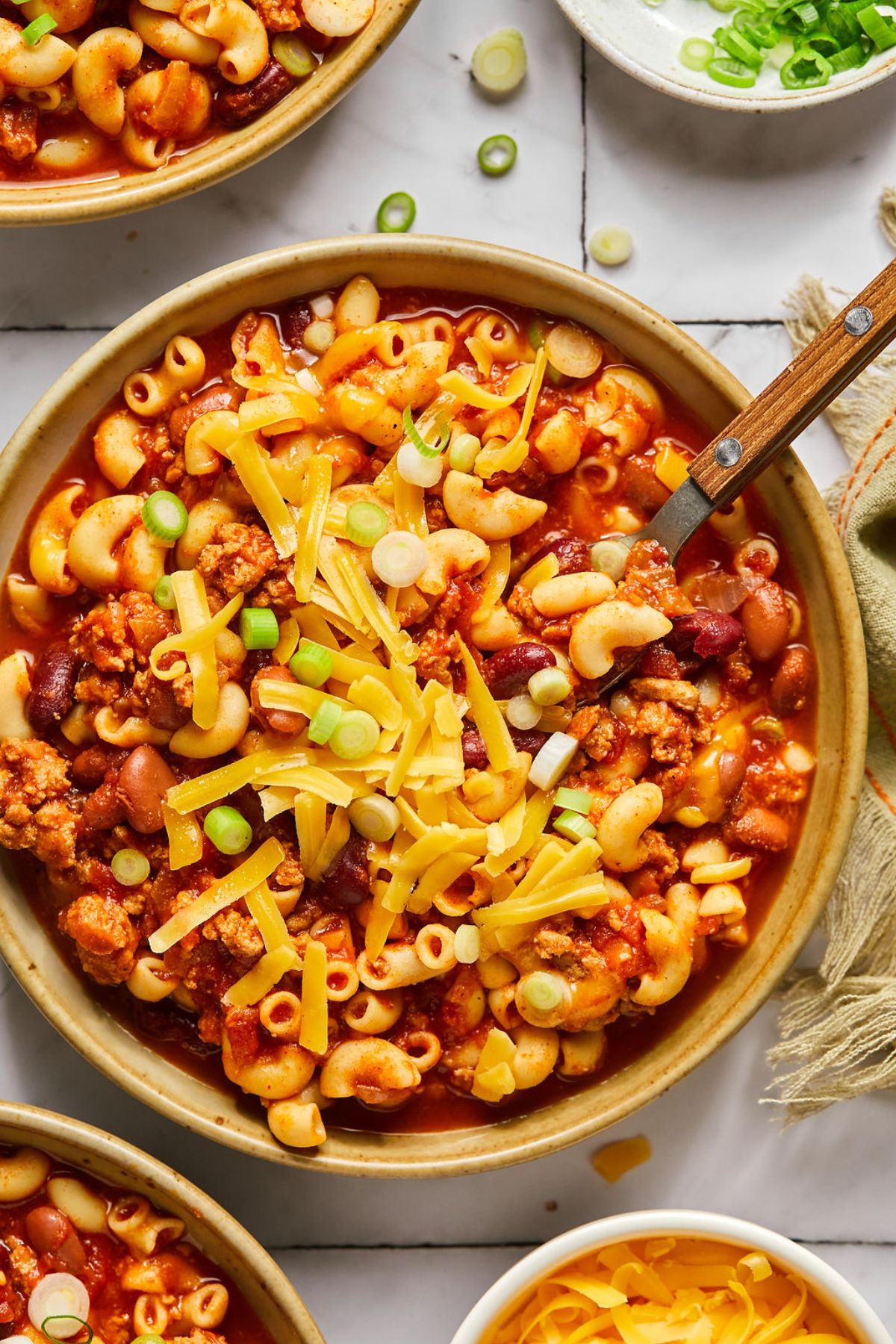 A bowl of healthy chili mac on the table with bowls of toppings around the edges.