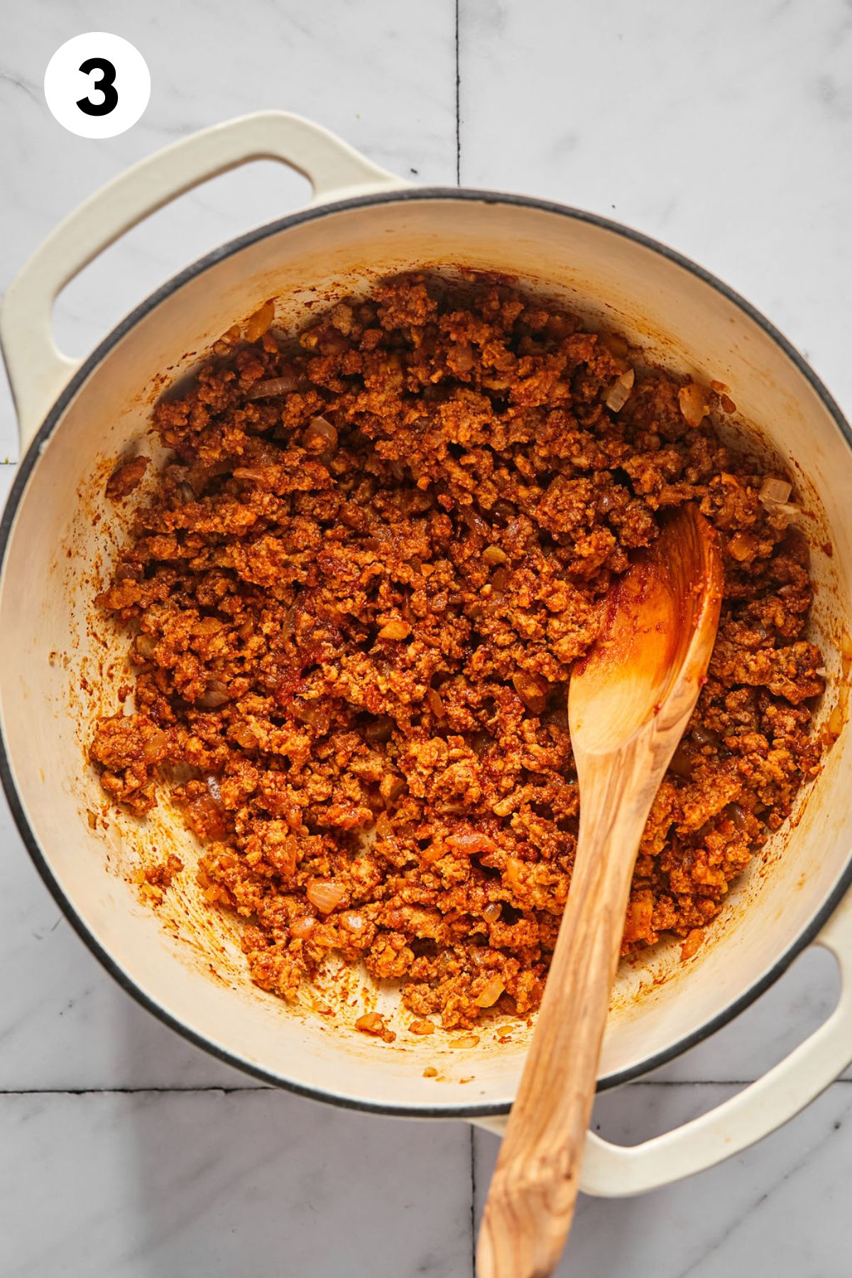 Tomato paste and spices cooked with the meat in a large pot with a wooden spoon resting in the pot.