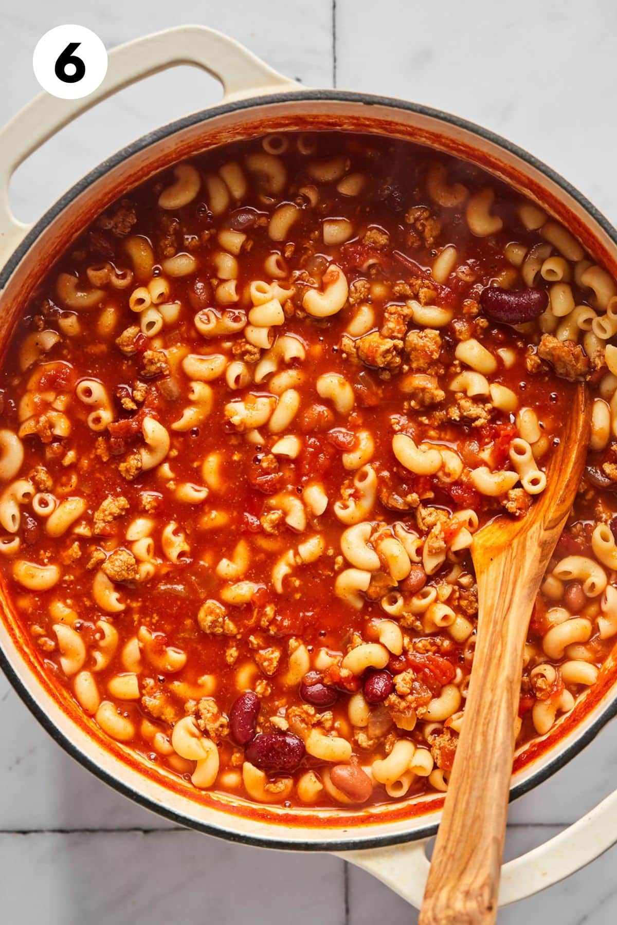 High protein chili mac cooked in a large pot with a wooden spoon resting in the dish.