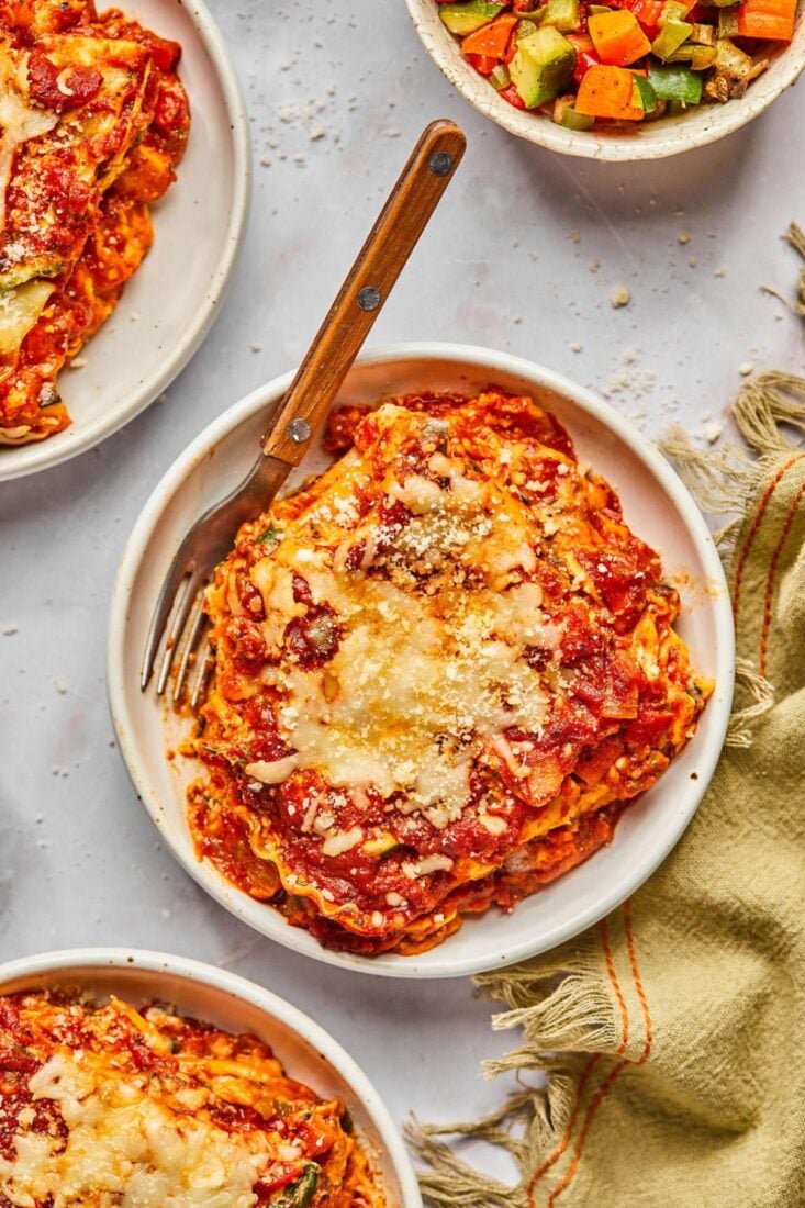 Plates of healthy vegetarian lasagna on a table with one in the middle with a fork resting on the plate.