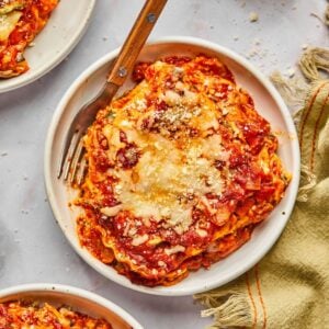 A slice of high protein vegetarian lasagna on a plate with a fork resting to the side.