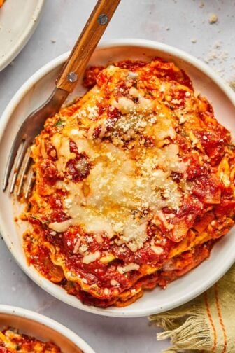 A slice of high protein vegetarian lasagna on a plate with a fork resting to the side.