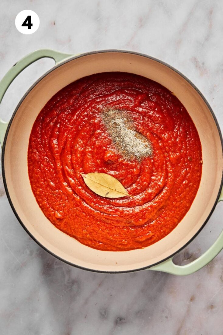 Tomato sauce added to the pot along with seasonings and a bay leaf.