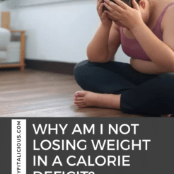 woman in a pink sports bra and black yoga pants sitting on the floor with her hands on her head.