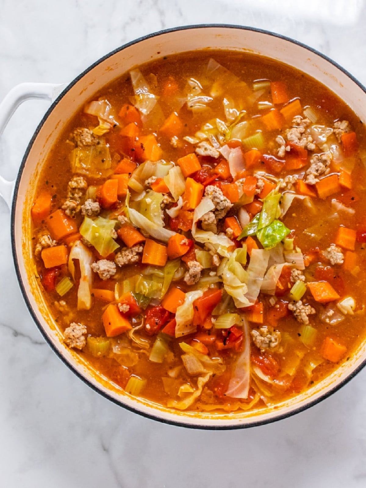 ground turkey, vegetables and cabbage soup in a large white pot.