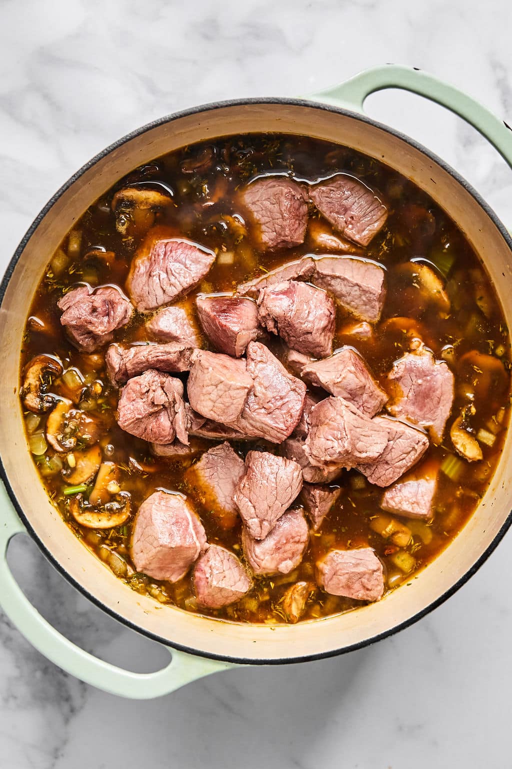 Browned beef added to the rest of the soup ingredients in the pot.