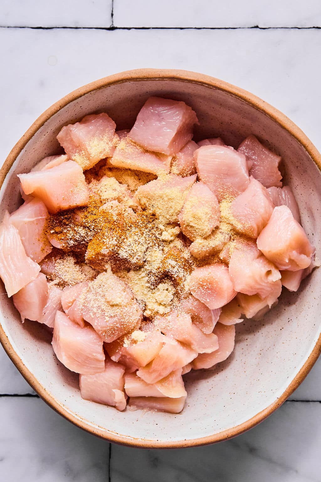 Chicken breast in cubes in a bowl with the seasonings added.