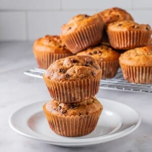 Two protein muffins stacked on a plate in front of a platter.