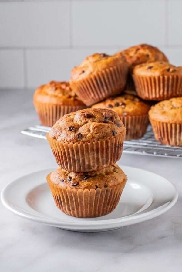 Two protein muffins stacked on a plate in front of a platter.