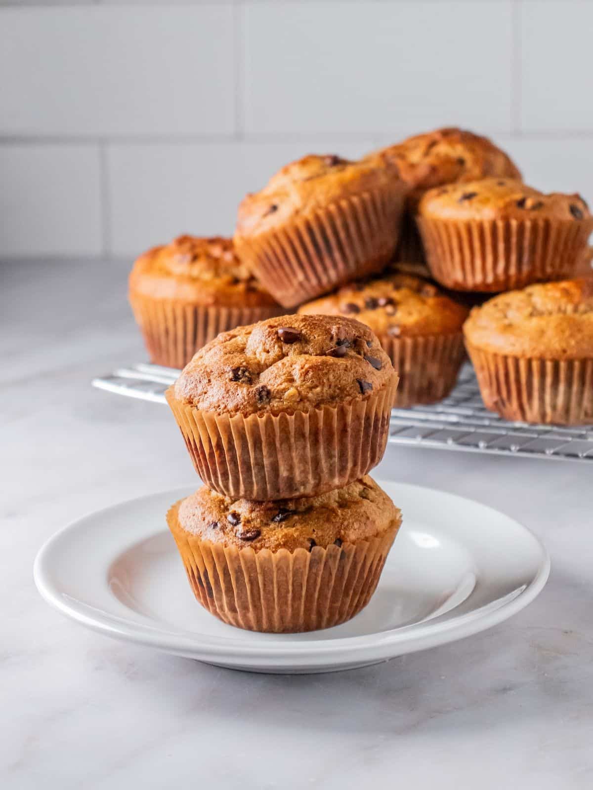 Two protein muffins stacked on a plate in front of a platter.