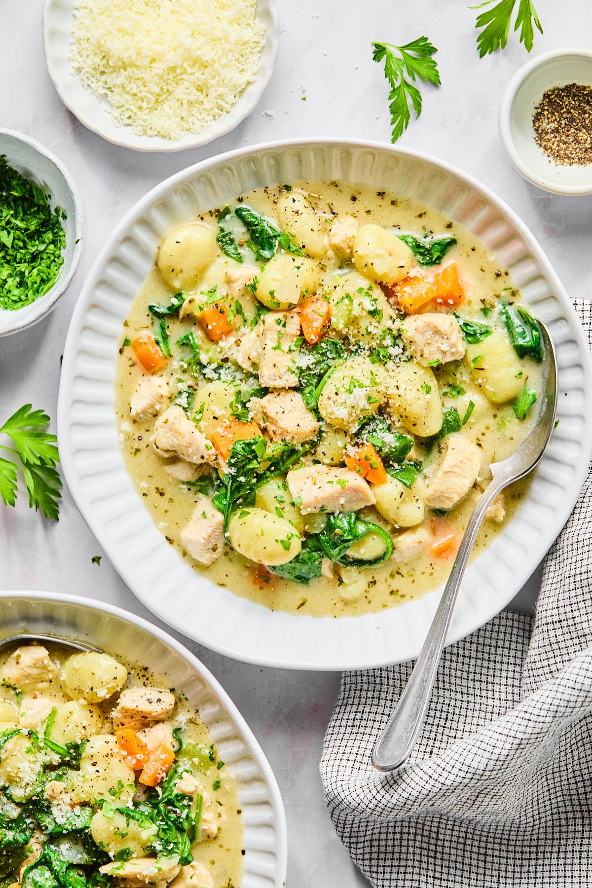 A bowl of creamy chicken gnocchi soup with a spoon in the bowl and a dish of Parmesan cheese to the side.