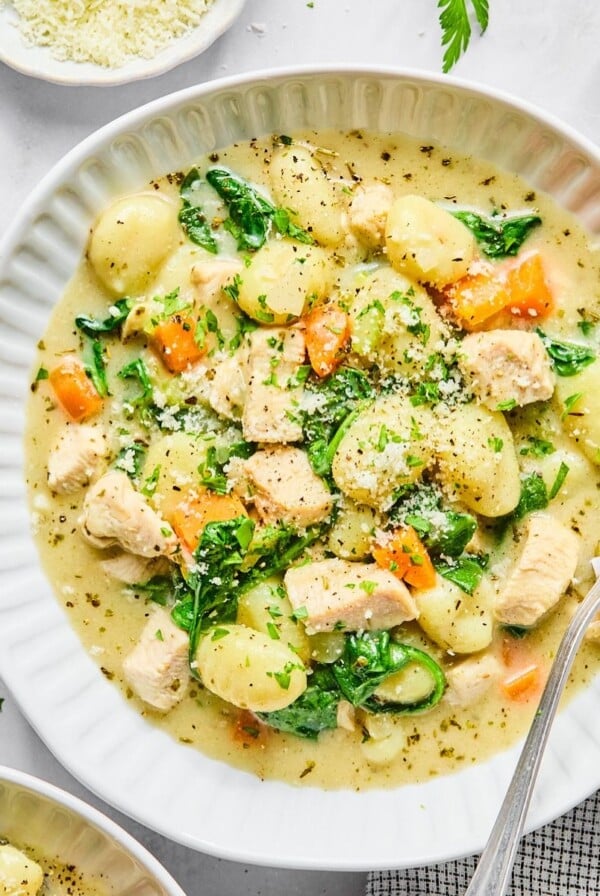 A bowl of creamy gnocchi soup with a spoon resting on the side.