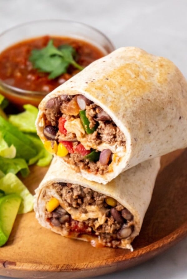 High protein burrito cut in half and stacked pn top of each next to a small salad.