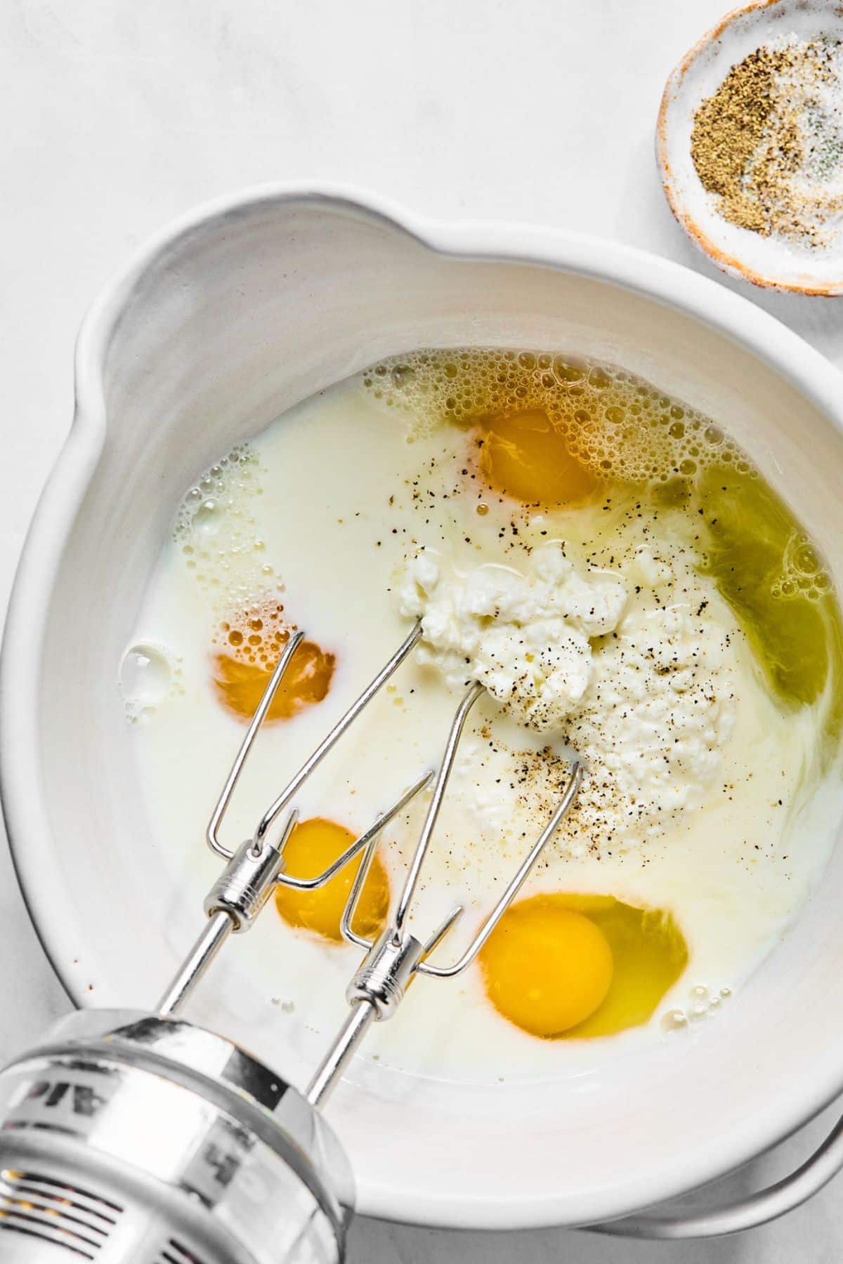 Eggs, milk and cottage cheese being mixed in a bowl.