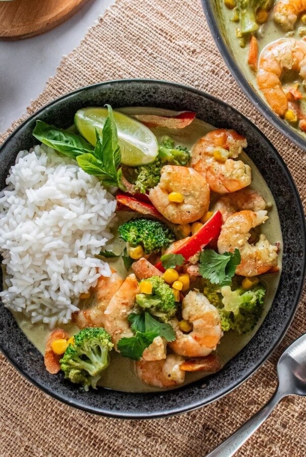 A bowl of shrimp curry recipe with a spoon to the side and the pot holding more.