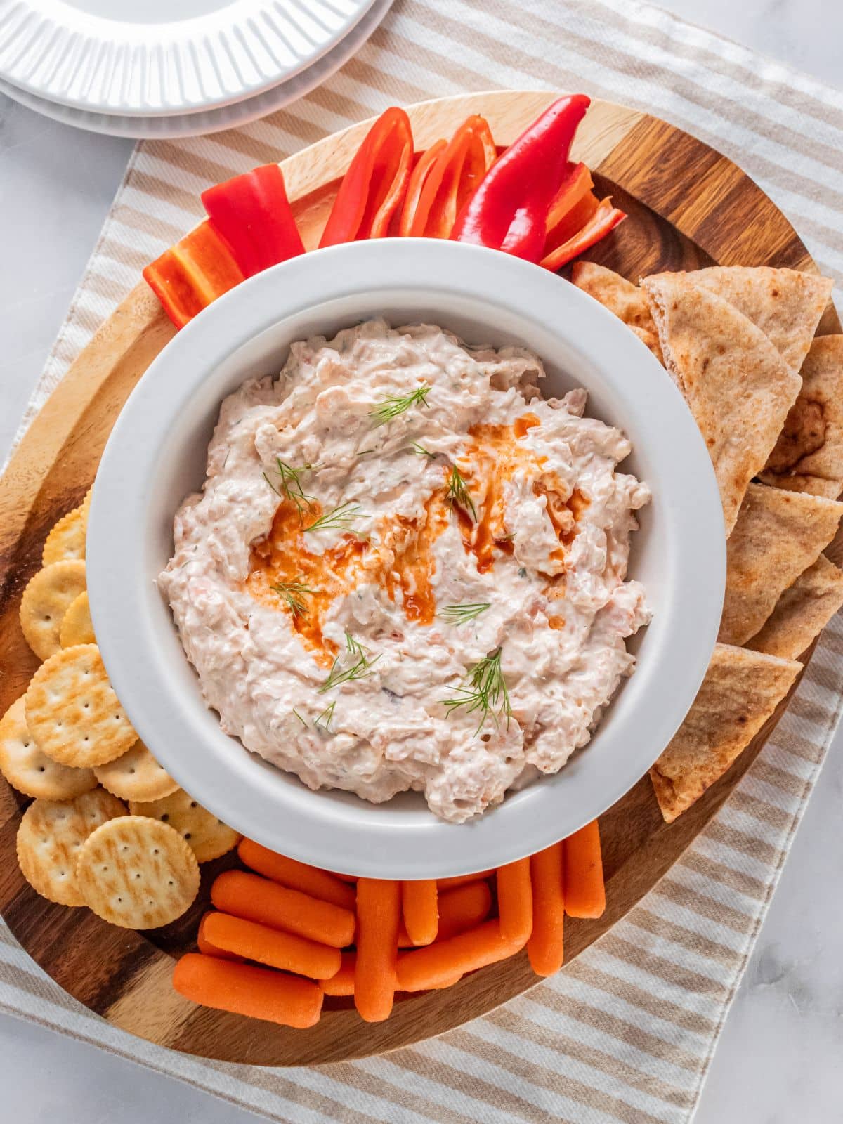 A dish of smoked salmon and cream cheese dip on a platter with vegetables and crackers on the side.