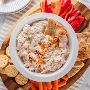 A bowl of smoked salmon dip surrounded by vegetable sticks and crackers.