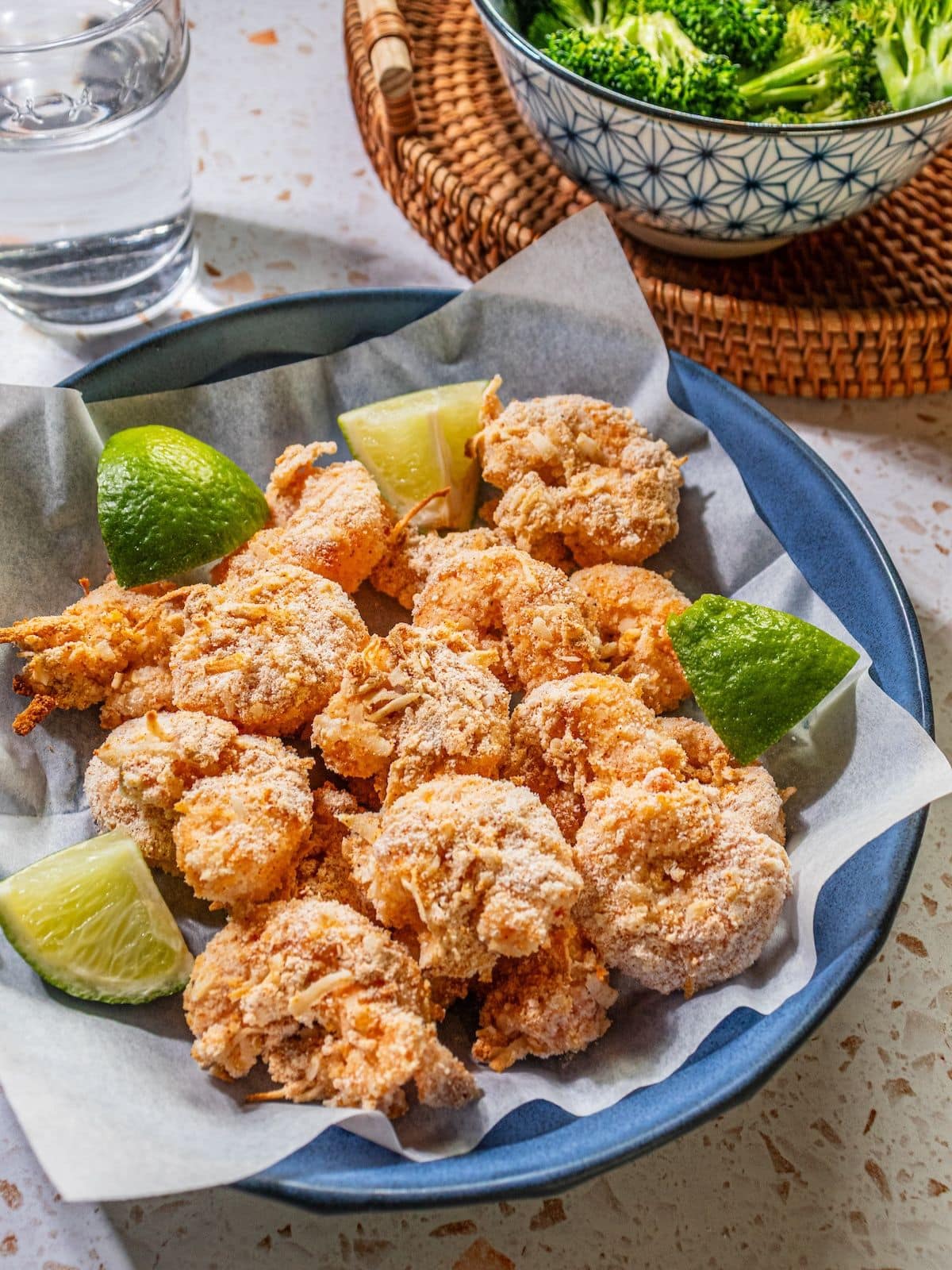 A blue bowl with baked coconut shrimp garnished with lime wedges. 