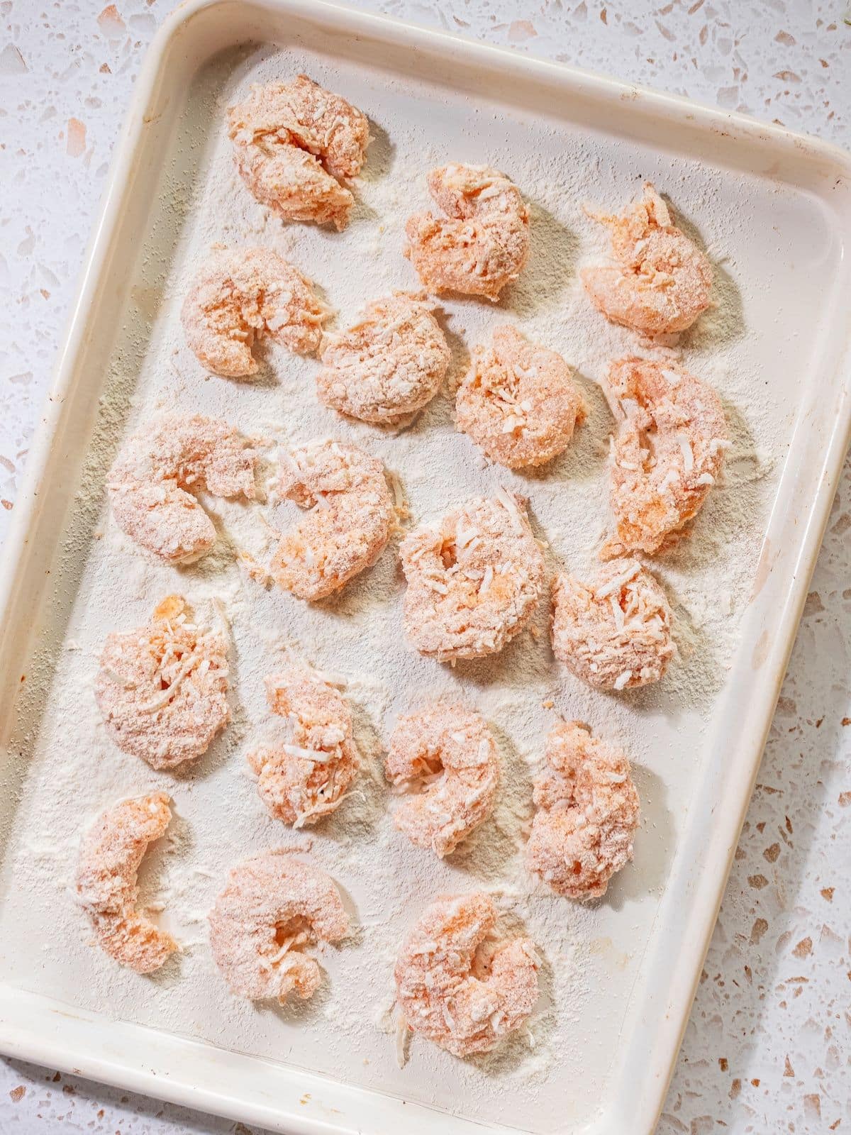Breaded shrimp laid down on the sheet pan.