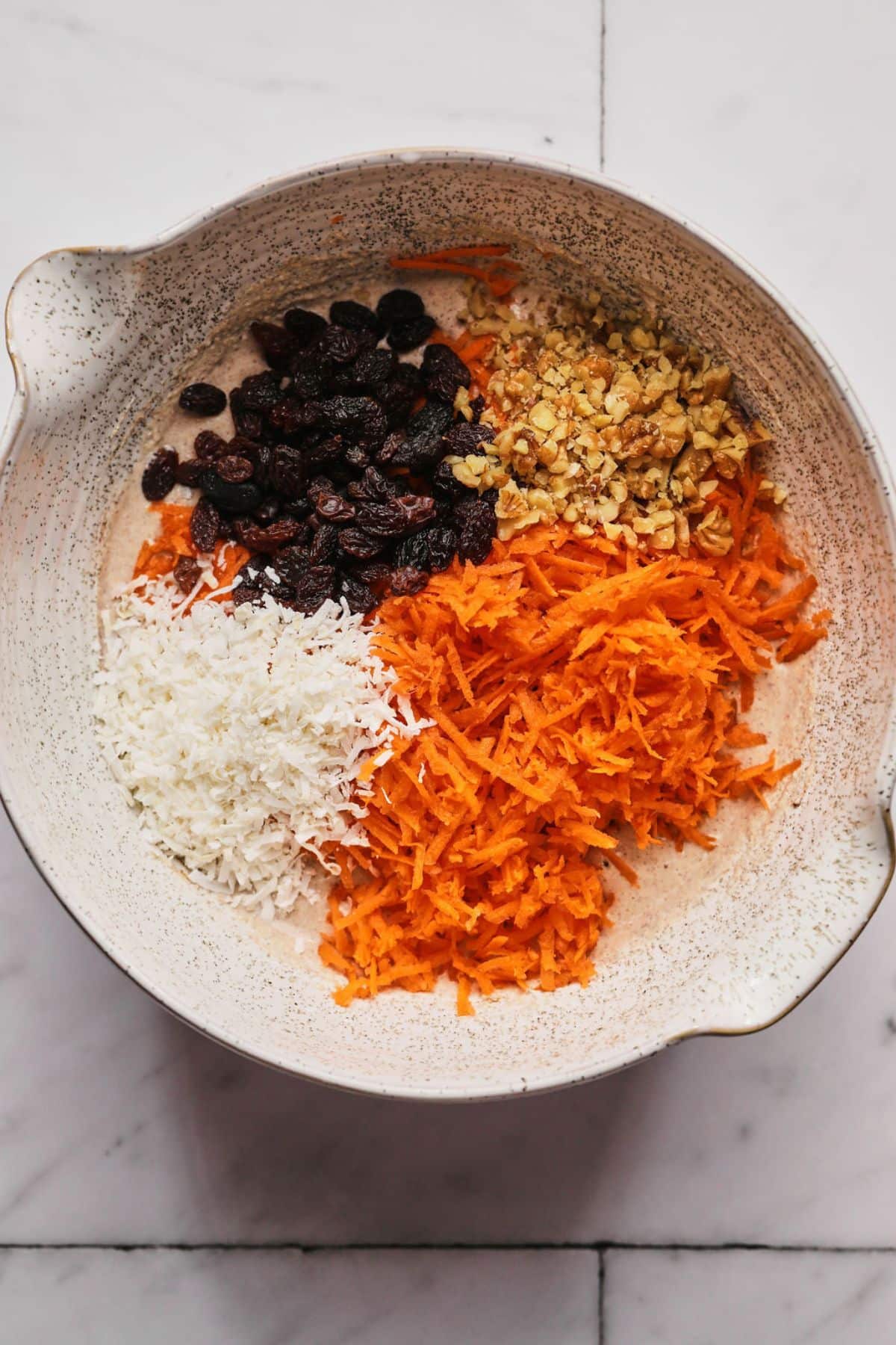 Baking soda, flour, cinnamon, nutmeg, raisins and unsweetened coconut flakes in a bowl.