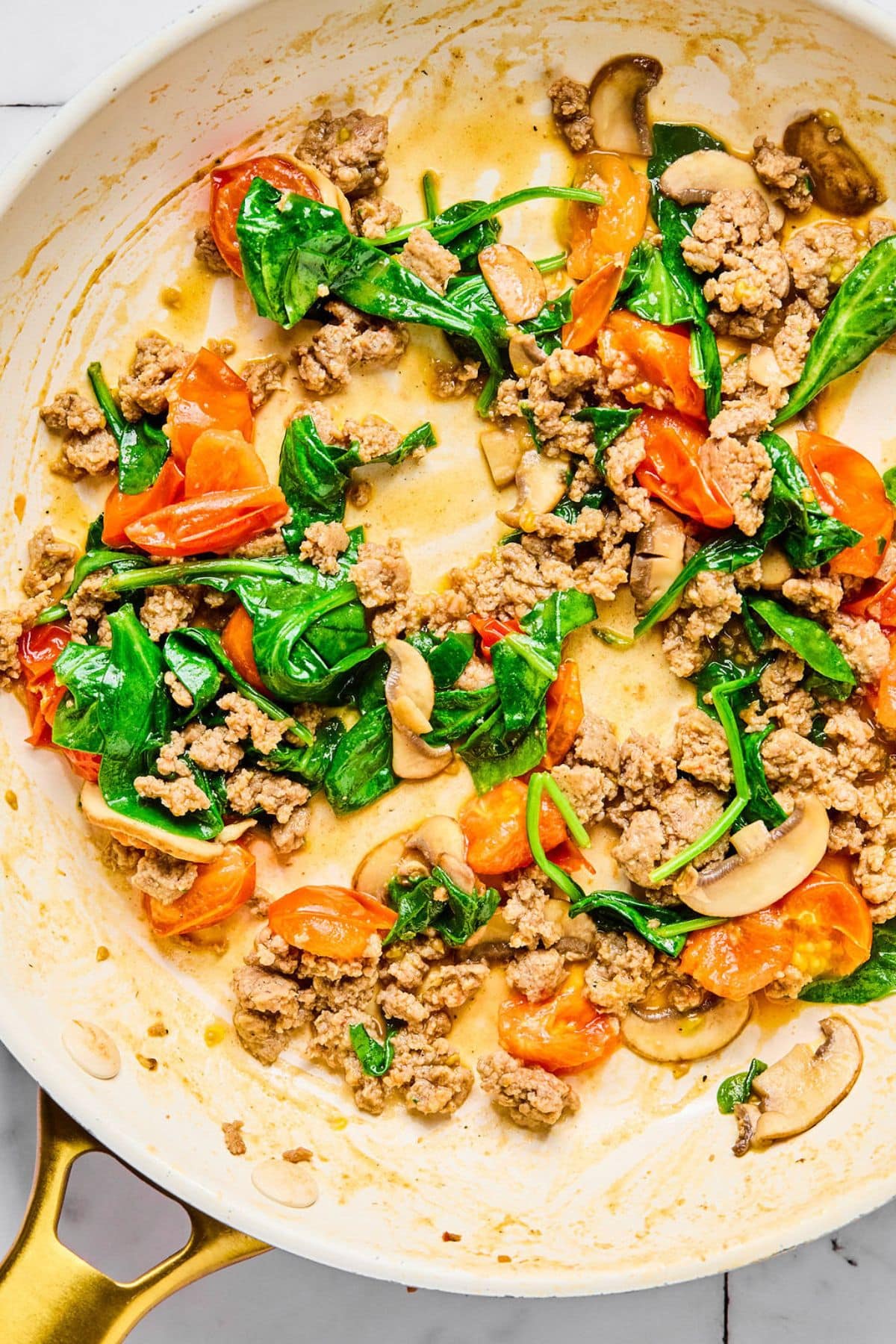 Turkey sausage, spinach, and tomatoes in a pan.