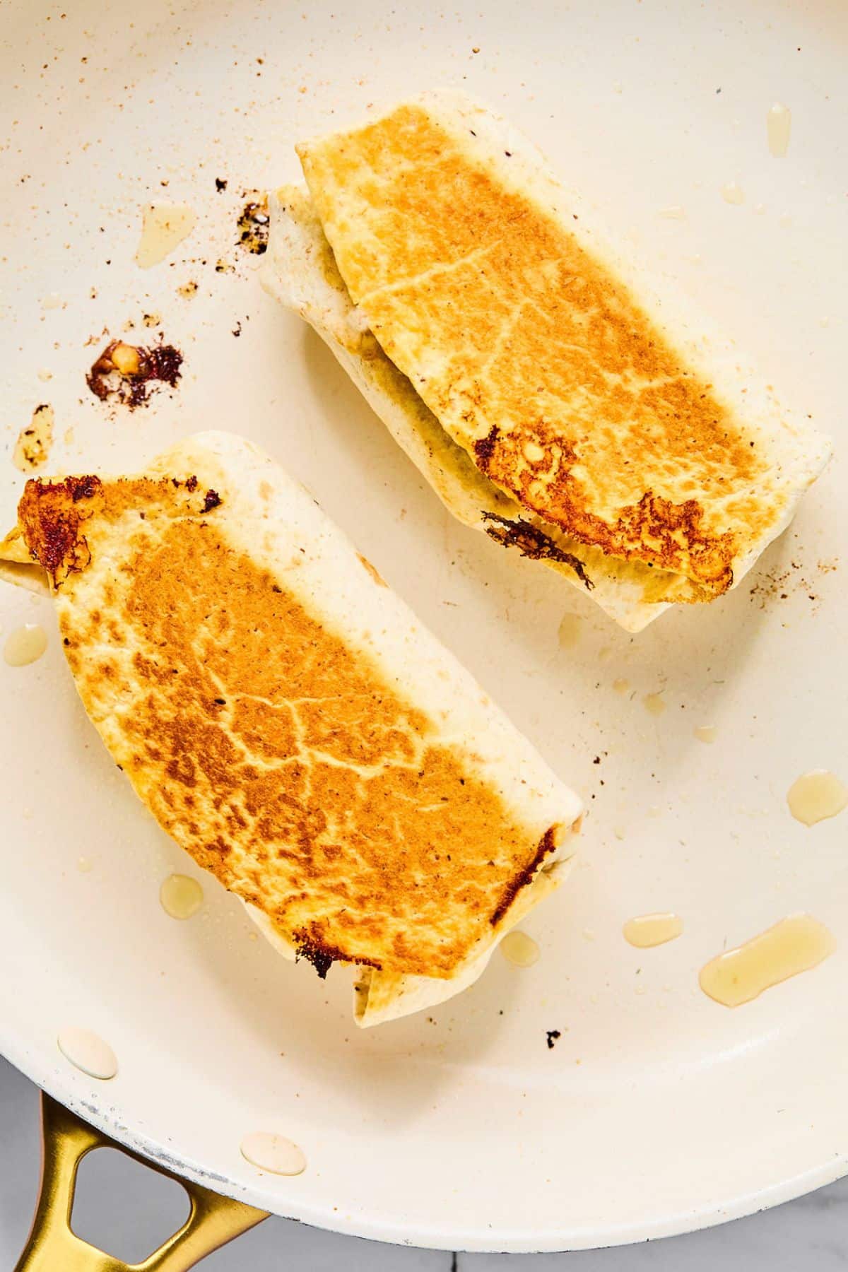 Two protein breakfast burritos toasting on a pan.