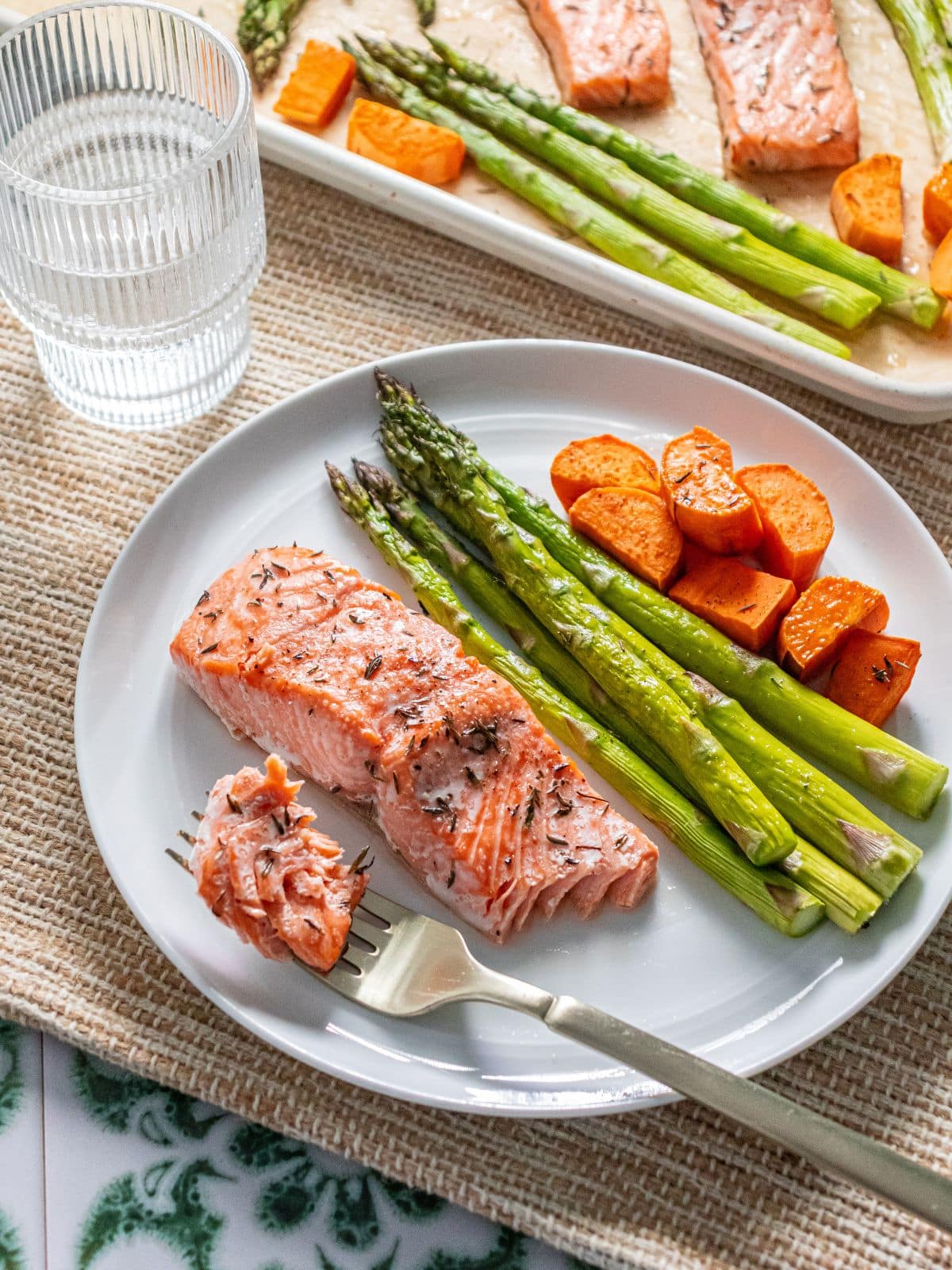 Salmon with asparagus and sweet potatoes on a plate and a bite of salmon on a fork.