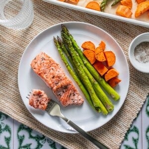 Sheet pan salmon on a plate with asparagus and sweet potatoes and a bite of salmon on a fork.