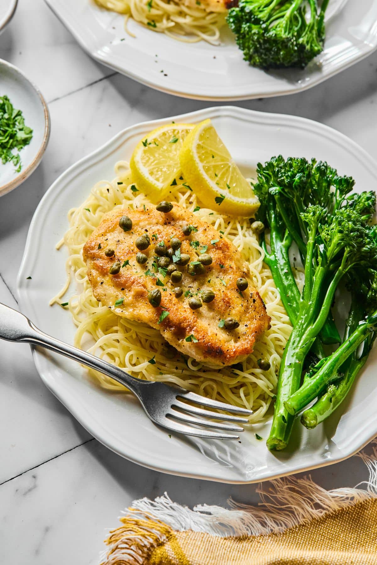 A plate with chicken piccata over pasta and a side of broccolini.