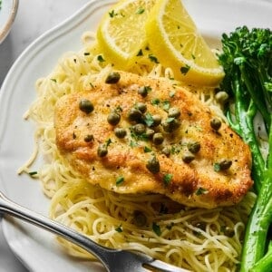 Healthy chicken piccata on a plate with pasta annd lemons on the side.