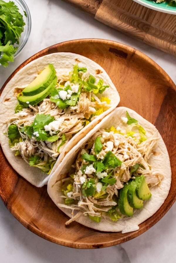 Two healthy chicken tacos with cheese, avocado and cilantro on top on a plate.