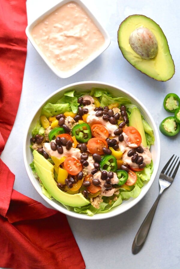 Taco salad in a bow with a side of sauce and half of an avocado.