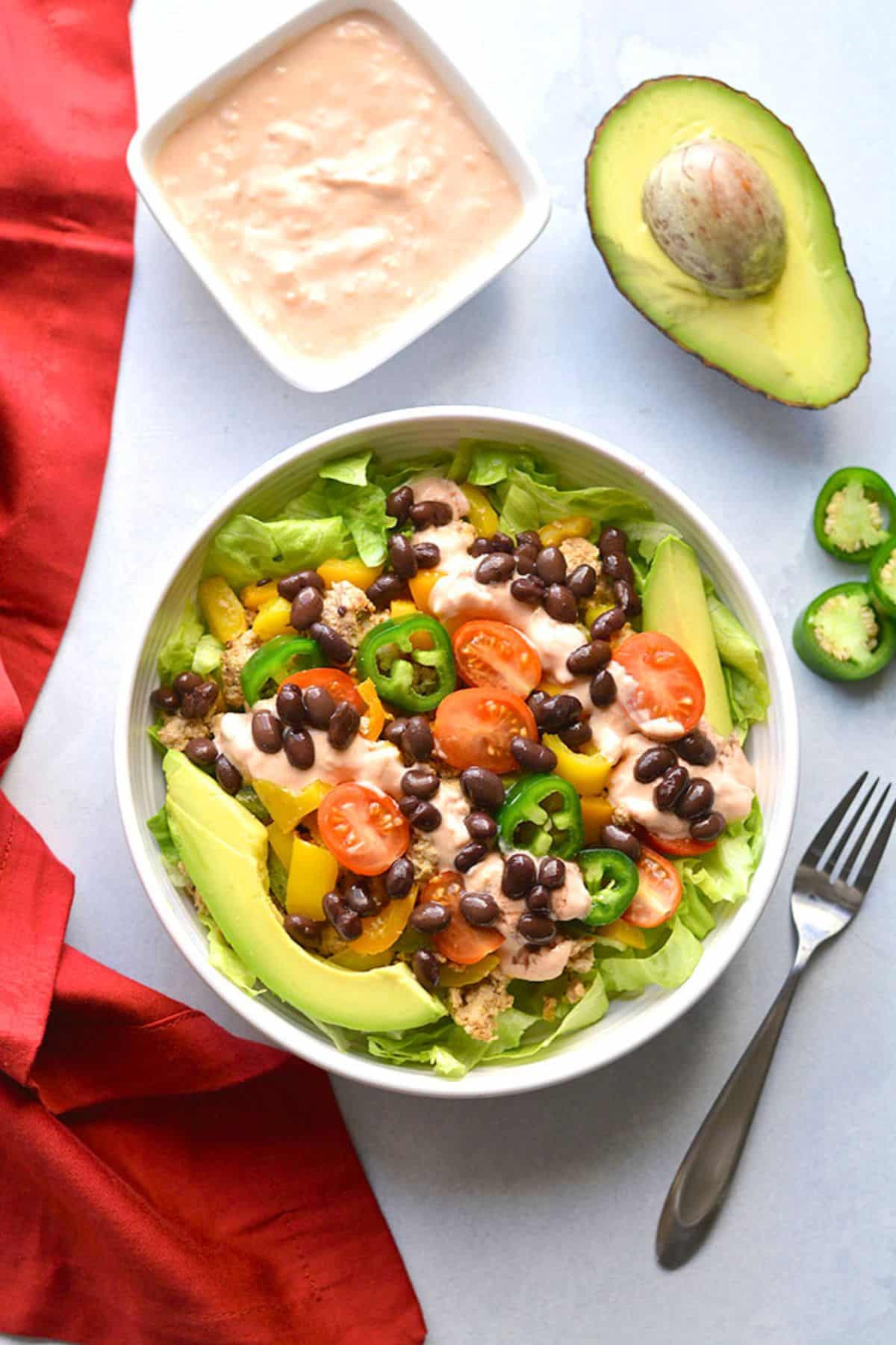 Healthy taco salad in a bowl with a side of sauce and half an avocado.