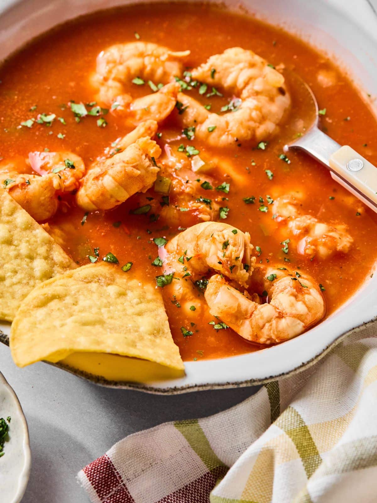 A spoon scooping out some soup with shrimp and tortilla chips.