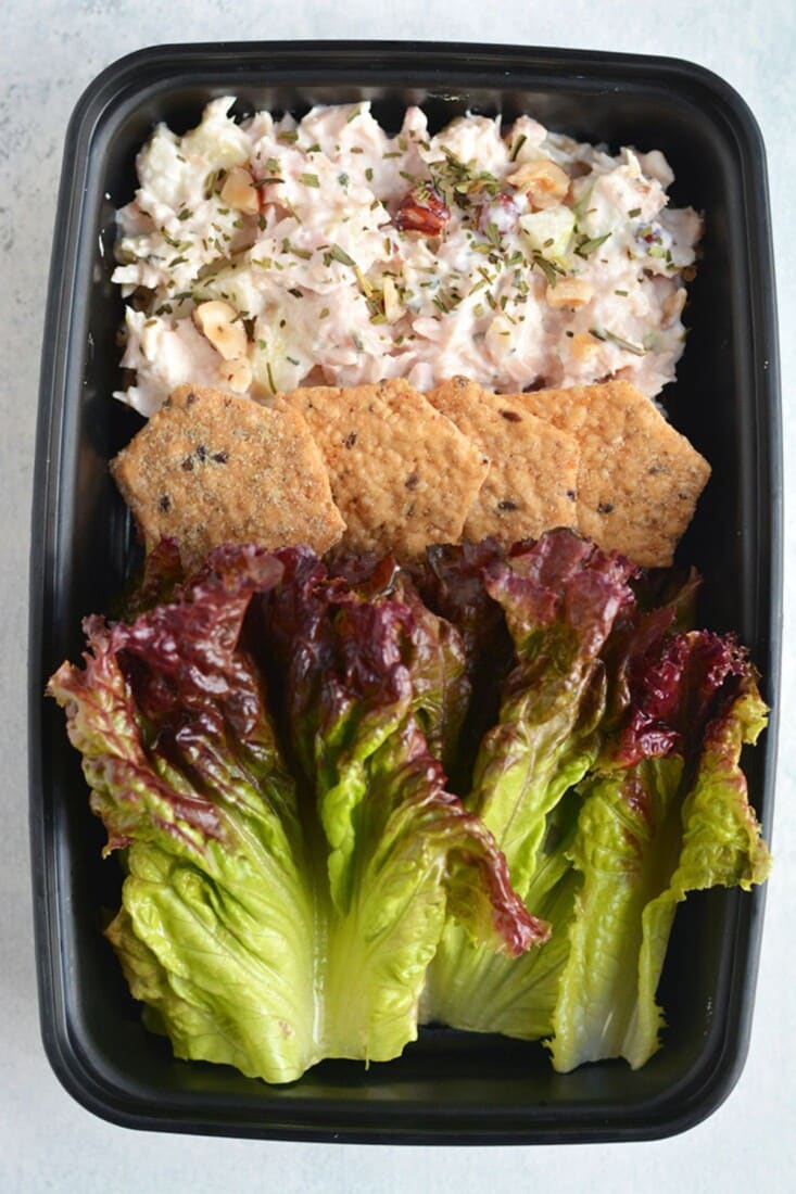 A plastic container with apple chicken salad, crackers and lettuce.