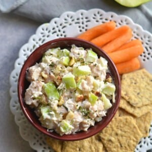 A plate with apple chicken salad, crackers and carrots.