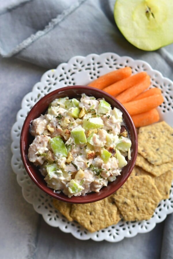 A plate with apple chicken salad, crackers and carrots.