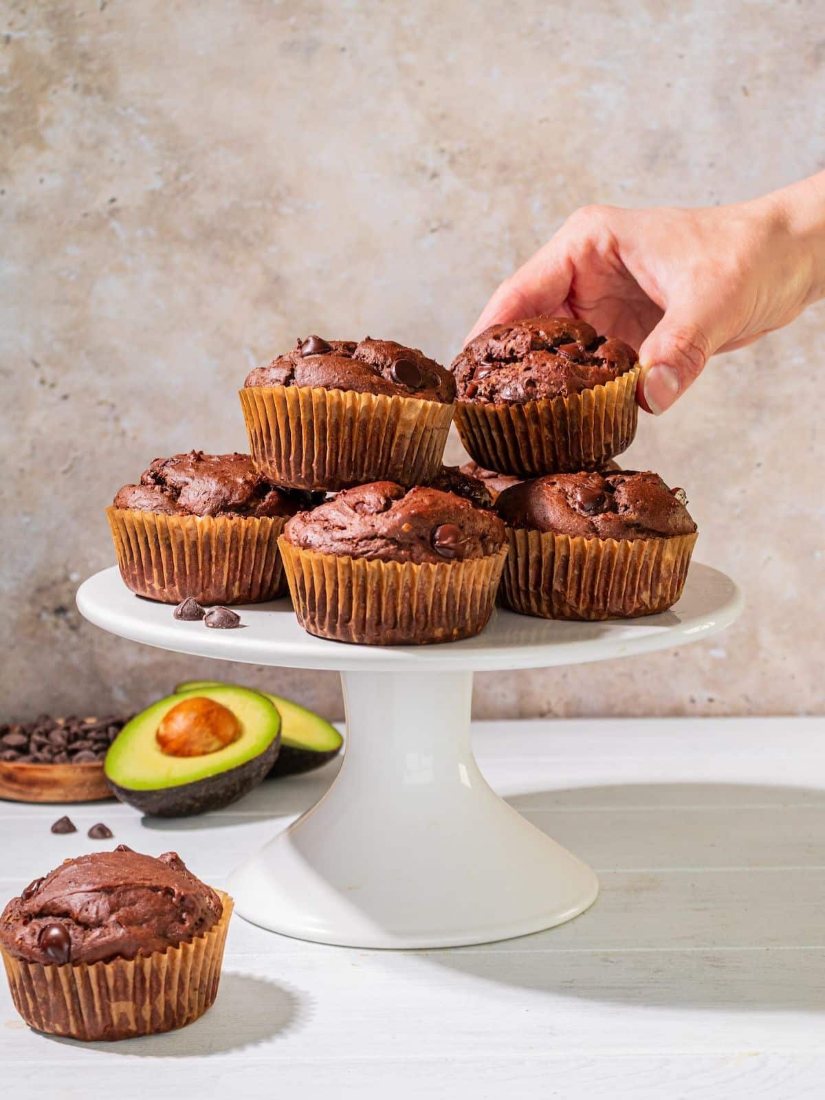 A hand taking a avocado chocolate muffin off of the cake plate.