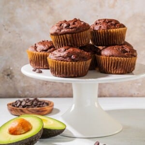 A bunch of chocolate avocado muffins stacked on a cake plate.