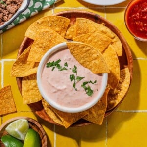 Creamy salsa dressing with a chip inside it and also around the bowl on a plate.