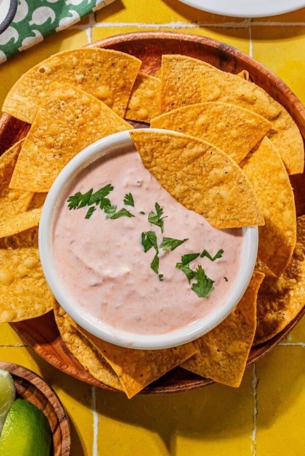 Creamy salsa dressing with a chip inside it and also around the bowl on a plate.