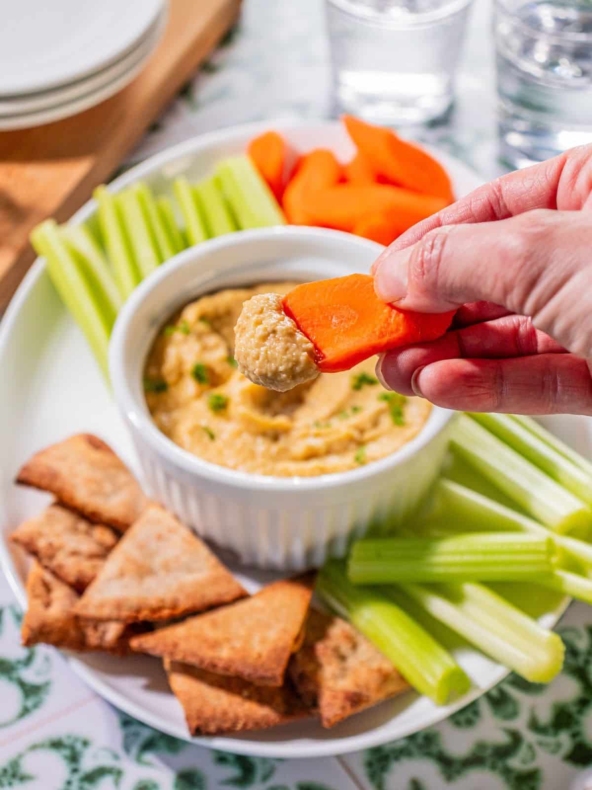 A carrot scooping up some garlic hummus.