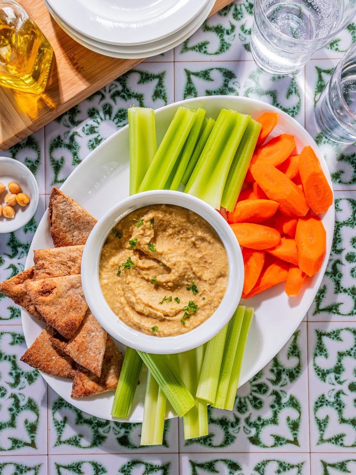 A plate with carrots, celery chips and hummus.